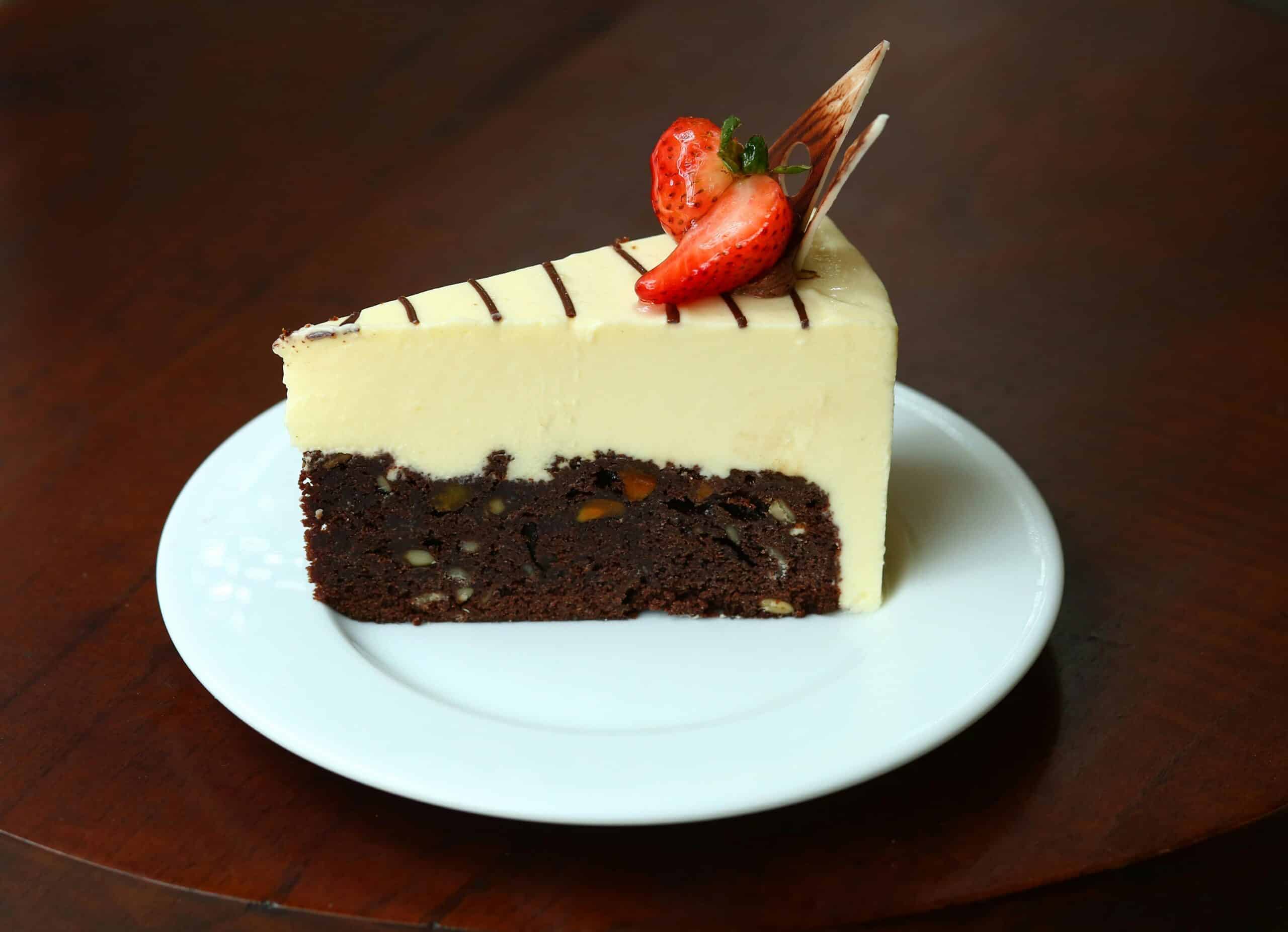 A slice of layered chocolate and cream cake topped with fresh strawberries and chocolate drizzle, served on a white plate.